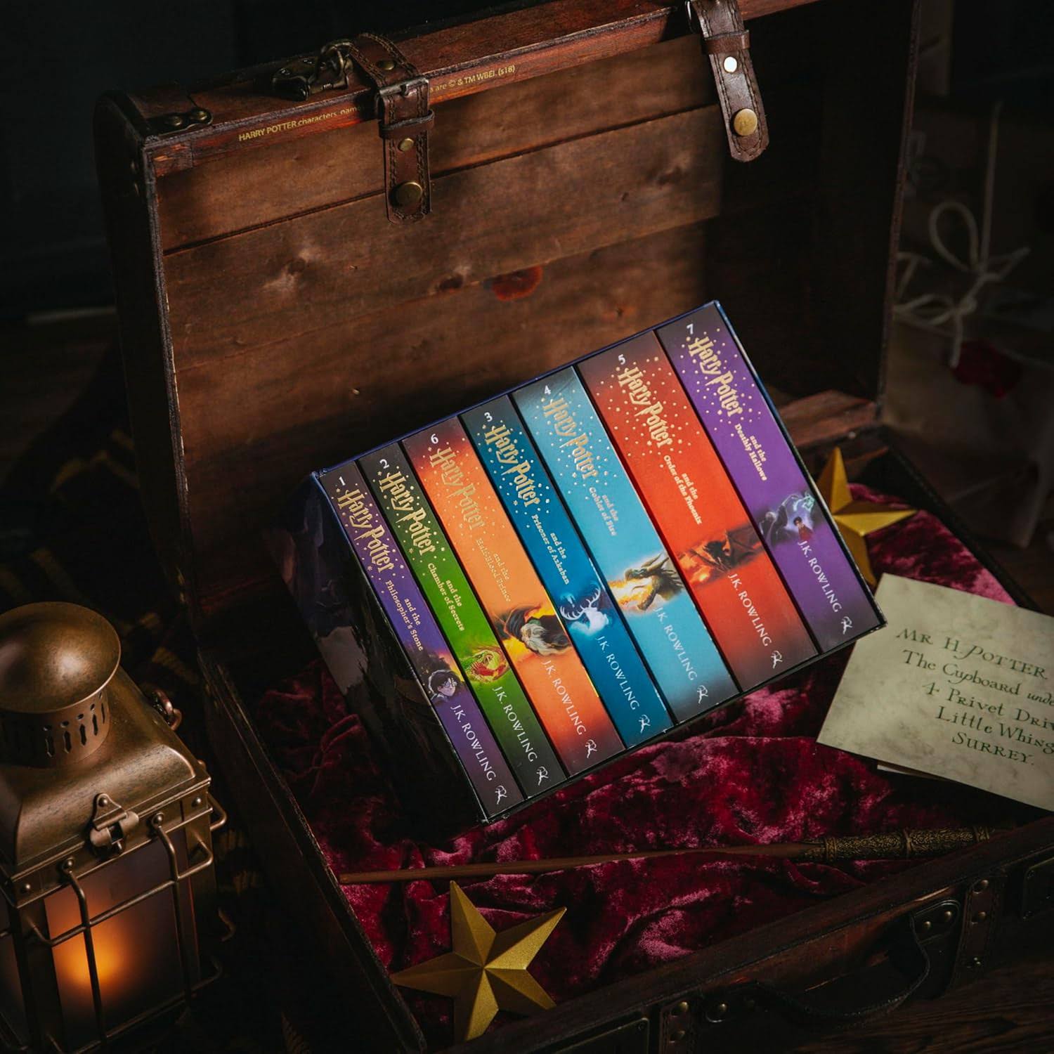 Harry Potter paperback box set by J.K. Rowling displayed in an open wooden chest with velvet lining, golden stars, and a Hogwarts-themed letter – magical gift setup.