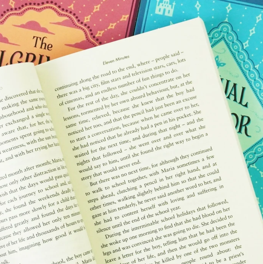 An open book spread showing printed text pages, with a decorative teal floral border on the right page and part of a warm orange cover visible at the top left.
