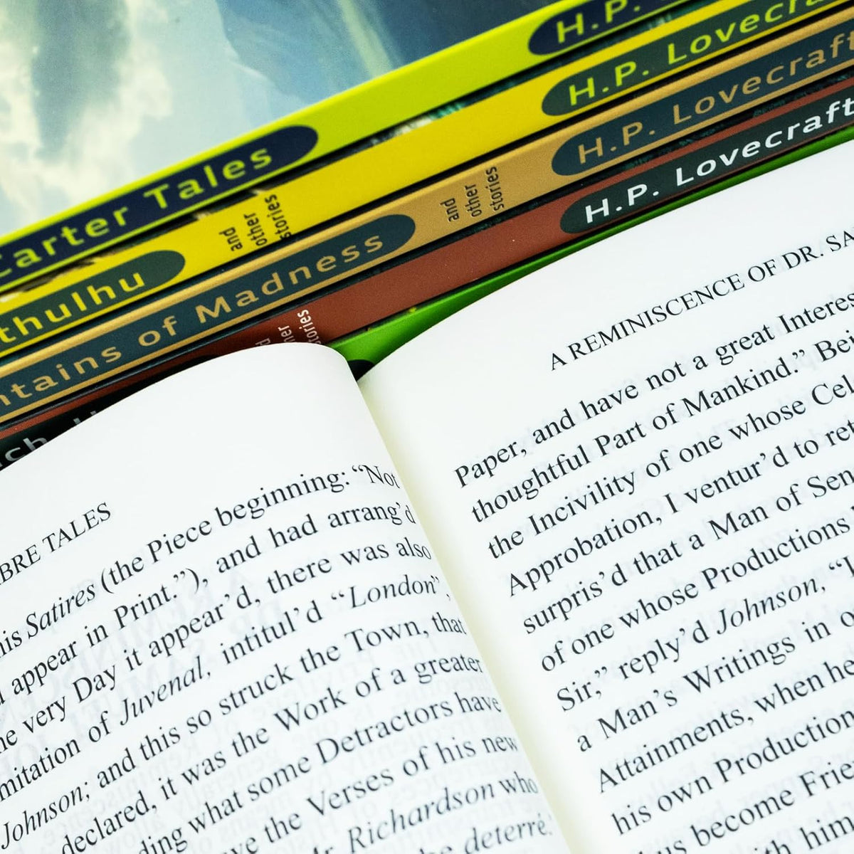 Stack of books with H.P. Lovecraft and other authors' titles, partially open to a page.