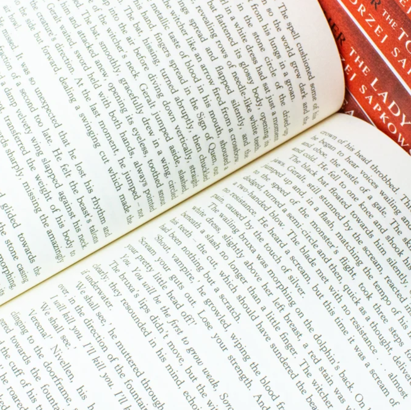 An open book spread with dense black text on cream pages, with two red books partially visible at the top right.