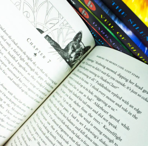 Open book with a bookmark featuring a wolf illustration, with other books stacked in the background.